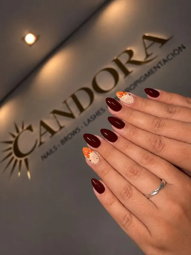 Manicura en tono burdeos con decoración, ante el rótulo de Candora en Móstoles